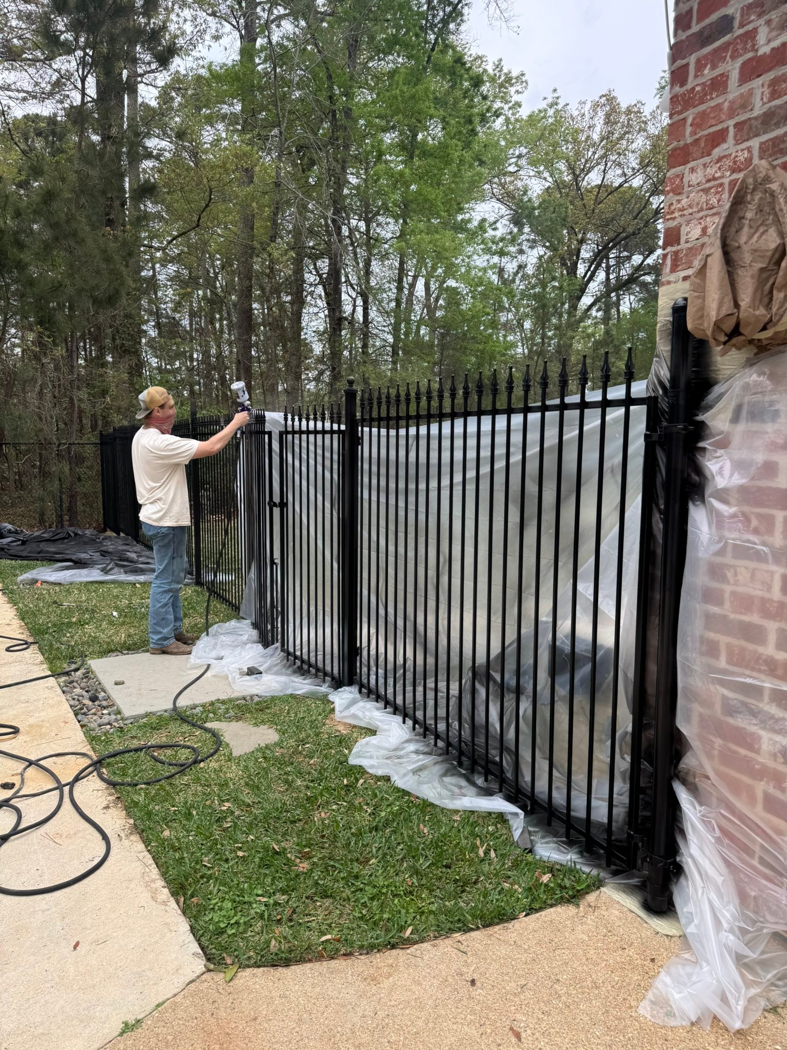 Fence contractor spray-finishing a black ornamental aluminum fence