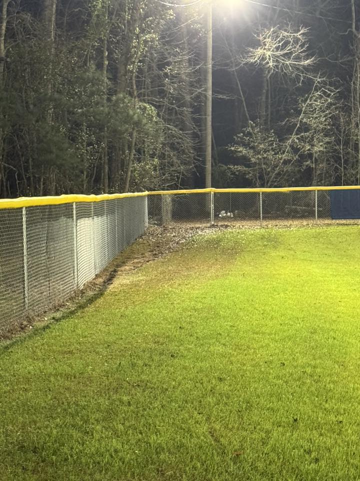 Chain link fence with yellow cap rail along a sports field
